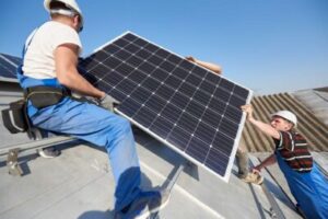 Workers lift a solar panel into place on a roof