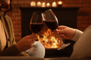 A couple toasting with their wine glasses in front of a fireplace